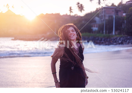 Young beautiful brunette girl with dreadlocks in a black dress on the beach Young beautiful brunette girl with dreadlocks in a black dress on the beach 53024117