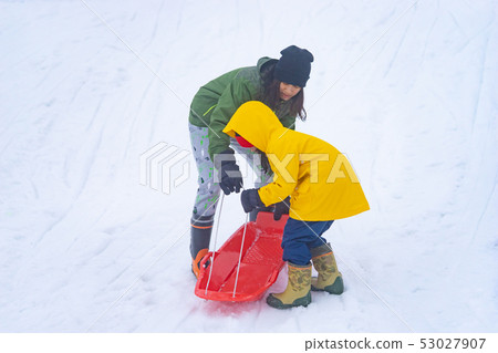 Mother is helping her daughter to ride the sled 53027907