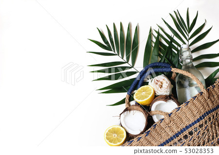 Summer still life composition with straw basket bag, lush palm leaves, lemons, coconut and glass Summer still life composition with straw basket bag, lush palm leaves, lemons, coconut and glass 53028353