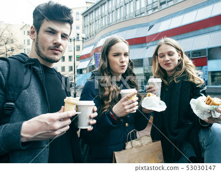lifestyle and people concept: two girls and guy eating fast food on city street together having fun 53030147