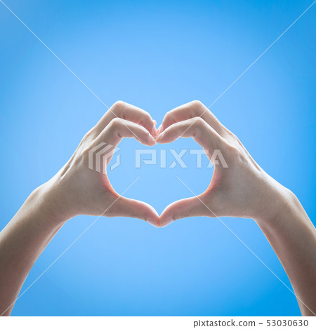 Heart shape woman hand raising against blue sky 53030630