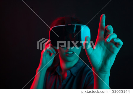 Cheerful beautiful young woman entertained with virtual reality helmet in studio and colorful 53055144