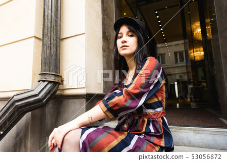 Elegant young woman in a multi-colored striped dress and black hat Elegant young woman in a multi-colored striped dress and black hat 53056872