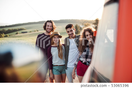 A group of young friends on a roadtrip through countryside, standing by a minivan. A group of young friends on a roadtrip through countryside, standing by a minivan. 53065396