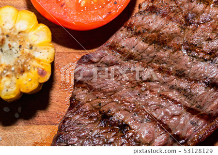 Close up freshly grilled steak on wood with tomatoes and corn 53128129