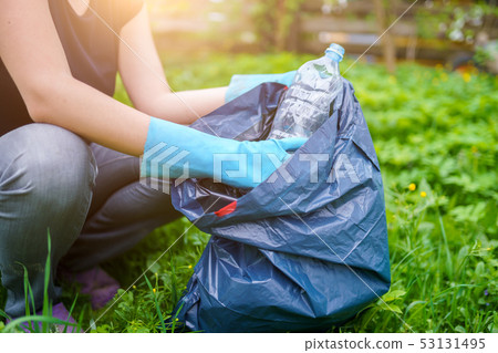 Image of woman in rubber gloves picking up dirty plastic bottle on lawn 53131495