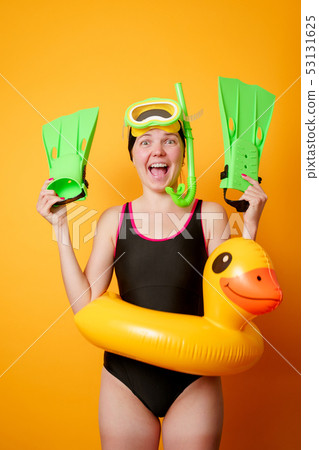 Photo of smiling woman with flippers in hands, swimming mask and with life preserver on empty orange Photo of smiling woman with flippers in hands, swimming mask and with life preserver on empty orange 53131625