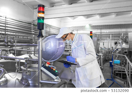 Inspector in a mask and a scrub stands with a folder-tablet in his hands at the dairy plant Inspector in a mask and a scrub stands with a folder-tablet in his hands at the dairy plant 53132090