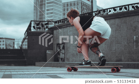 Beautiful young girl with tattoos sits on longboard 53133418