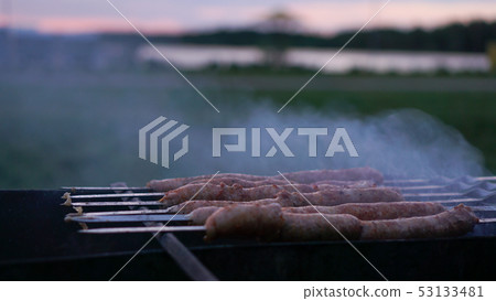 Grilling sausages at sunset outdoors gathering with friends and family Grilling sausages at sunset outdoors gathering with friends and family 53133481