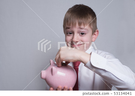 Happy boy puts a coin in a pink piggy bank. Happy boy puts a coin in a pink piggy bank. 53134041