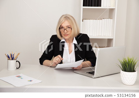Business lady in office holding paper documents and smiling. Business lady in office holding paper documents and smiling. 53134156