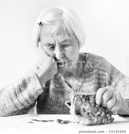 Elderly woman sitting at the table counting money in her wallet. 53134309