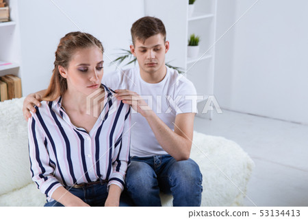 At the psychologist. Beautiful young couple is sitting on couch and hugging while doctor is making 53134413