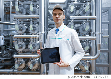 Portrait of man in a white robe and a cap standing in production department of dairy factory with Portrait of man in a white robe and a cap standing in production department of dairy factory with 53147215