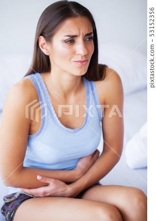 Stomach Pain. Unhealthy young woman with stomachache leaning on the bed at home 53152356