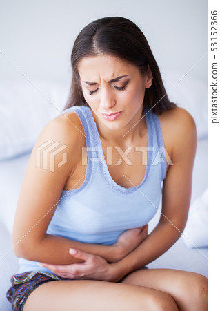 Stomach Pain. Unhealthy young woman with stomachache leaning on the bed at home 53152366