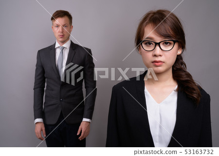 Young businessman and young Asian businesswoman against gray bac Young businessman and young Asian businesswoman against gray bac 53163732