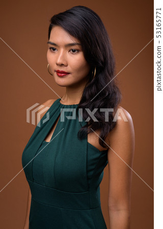 Studio shot of beautiful Asian businesswoman against brown backg Studio shot of beautiful Asian businesswoman against brown backg 53165771