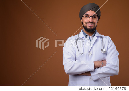 Young bearded Indian Sikh man doctor wearing turban against brow Young bearded Indian Sikh man doctor wearing turban against brow 53166278
