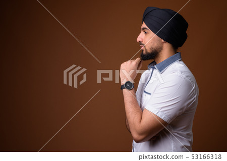 Young bearded Indian Sikh man wearing turban against brown backg Young bearded Indian Sikh man wearing turban against brown backg 53166318