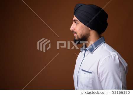 Young bearded Indian Sikh man wearing turban against brown backg Young bearded Indian Sikh man wearing turban against brown backg 53166320