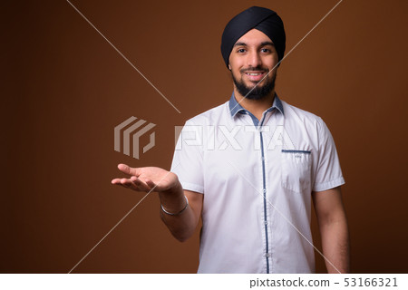 Young bearded Indian Sikh man wearing turban against brown backg Young bearded Indian Sikh man wearing turban against brown backg 53166321