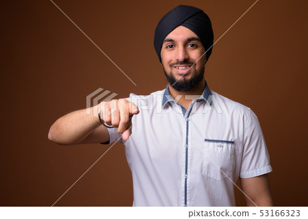Young bearded Indian Sikh man wearing turban against brown backg Young bearded Indian Sikh man wearing turban against brown backg 53166323