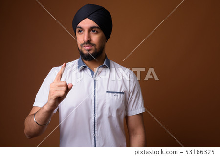 Young bearded Indian Sikh man wearing turban against brown backg Young bearded Indian Sikh man wearing turban against brown backg 53166325