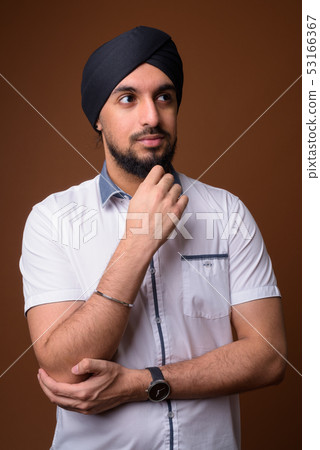 Young bearded Indian Sikh man wearing turban against brown backg Young bearded Indian Sikh man wearing turban against brown backg 53166367