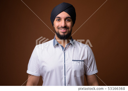 Young bearded Indian Sikh man wearing turban against brown backg 53166368