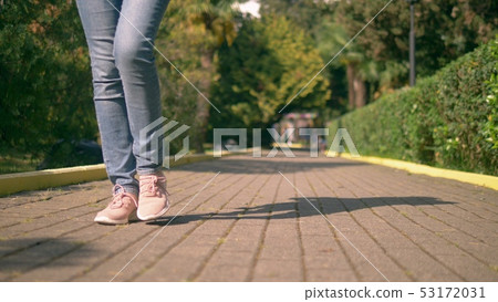 women's legs in jeans and sneakers are on a paved path women's legs in jeans and sneakers are on a paved path 53172031