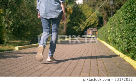 women's legs in jeans and sneakers are on a paved path women's legs in jeans and sneakers are on a paved path 53172032