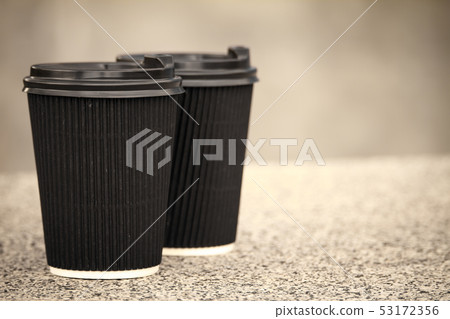 Two black disposable cups of coffee with lids are Two black disposable cups of coffee with lids are 53172356