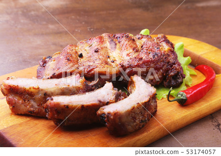 grilled barbecued ribs with lettuce leaves, hot chili pepper and sauce on wooden cutting board. 53174057