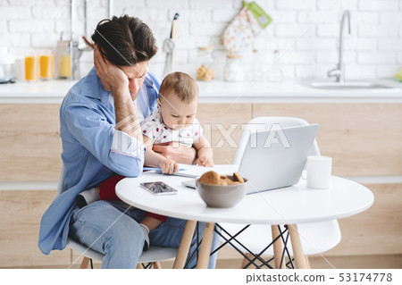 Exhausted young man napping at kitchen, baby son playing with notes 53174778