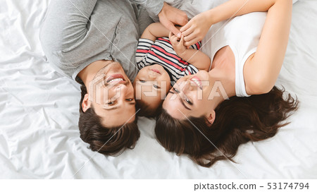 Adorable baby lying in bed with parents, having fun Adorable baby lying in bed with parents, having fun 53174794