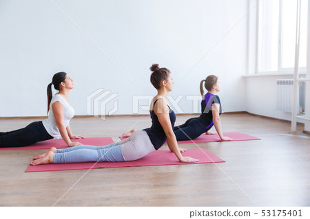 Three young girls doing yoga in a large bright room with a large window. Three young girls doing yoga in a large bright room with a large window. 53175401