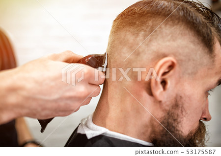 Master cuts hair and beard of men in the barbershop, hairdresser makes hairstyle for a young man 53175587
