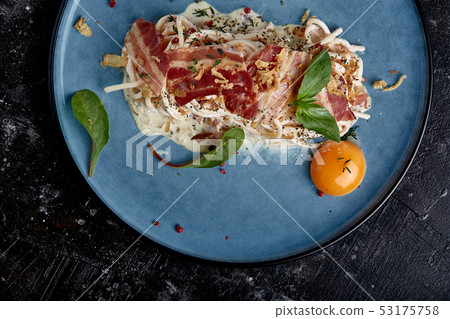 Classic pasta carbonara with yolk on a plate. Pasta laid out on a blue plate on a dark background 53175758