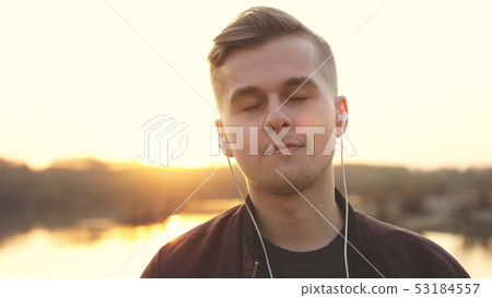 Young handsome man closed eyes listens to music on beach during sunset. 53184557