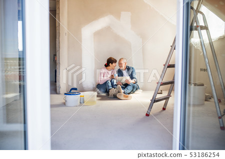 Senior couple painting walls in new home, using tablet. Relocation concept. Senior couple painting walls in new home, using tablet. Relocation concept. 53186254