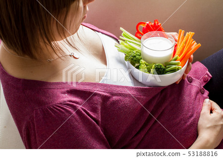 Pregnant female holding vegetable sticks and dip Pregnant female holding vegetable sticks and dip 53188816