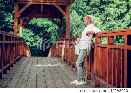 Stylish aged lady leaning on the brown wooden bridge Stylish aged lady leaning on the brown wooden bridge 53192610