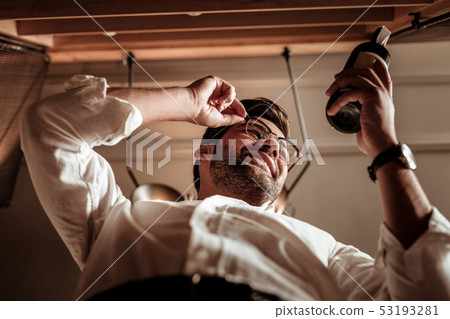 Low angle photo of bearded man that looking at bottle 53193281