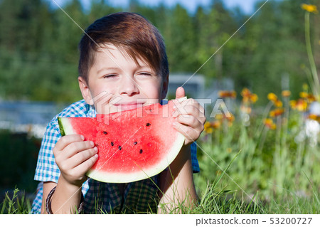 Funny boy eats watermelon outdoors in summer park Funny boy eats watermelon outdoors in summer park 53200727