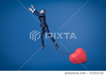 Side view of businessman in mid-air chained to big Valentine heart on the ground. Side view of businessman in mid-air chained to big Valentine heart on the ground. 53202216