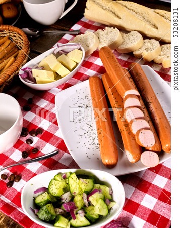 Sausage portion with baguette on table setting on checkered cloth 53208131