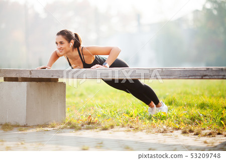Portrait of beautiful sporty woman 20s in sportswear doing push-ups, and listening to music with 53209748