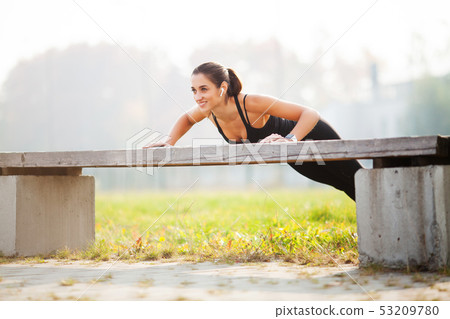 Portrait of beautiful sporty woman 20s in sportswear doing push-ups, and listening to music with 53209780